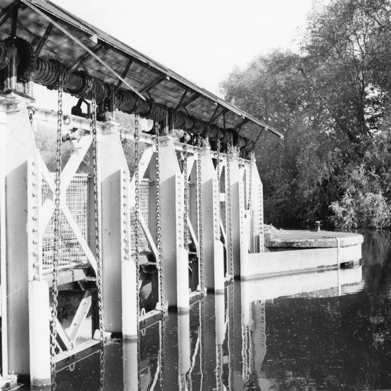 the large metal weir mechanism on the River Thames at Abingdon, reflected in the water on a still morning.