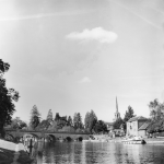 A black and white photograph of an old bridge across the river Thames at Wallingford, Oxfordshire. The spires of a town are in the background and boats are moored on the river banks